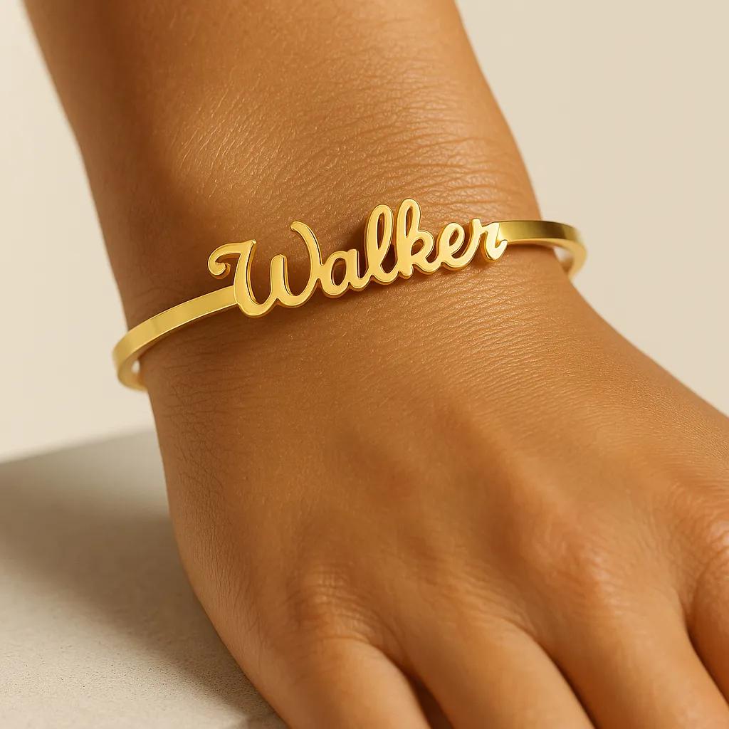 Gold bracelet with 'Walker' engraving on a wrist against a beige background