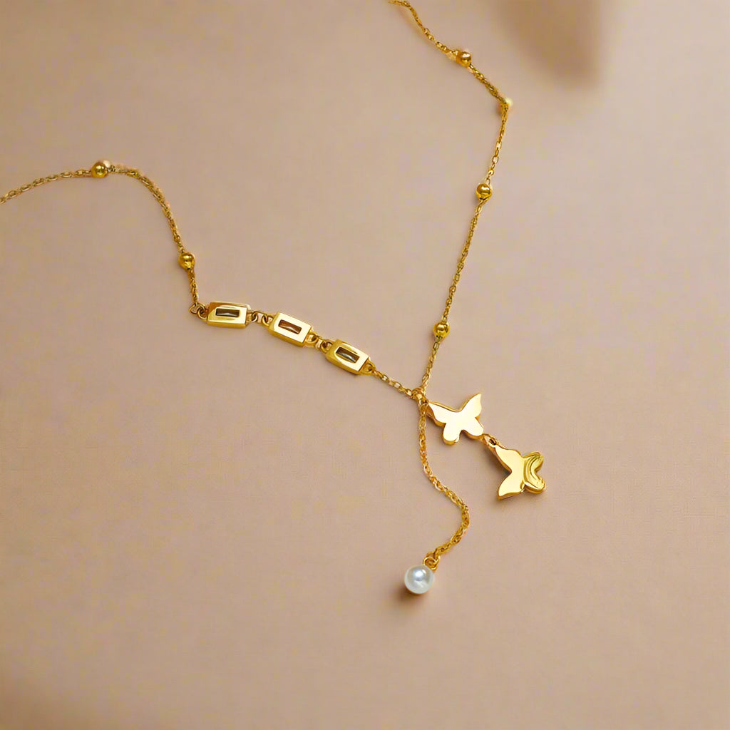 Double butterfly pendant necklace in gold, displayed on a beige jewelry box