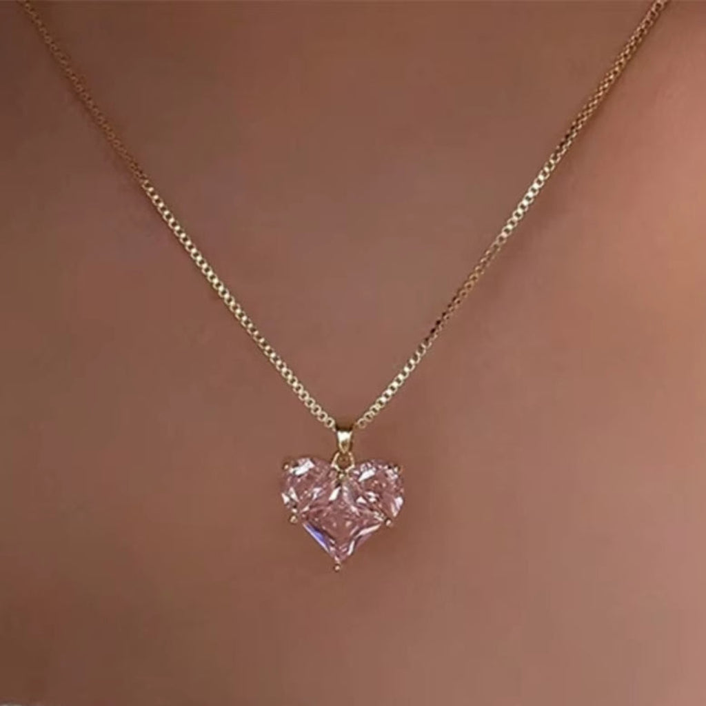 Gold necklace with a pink heart-shaped pendant on a neutral background