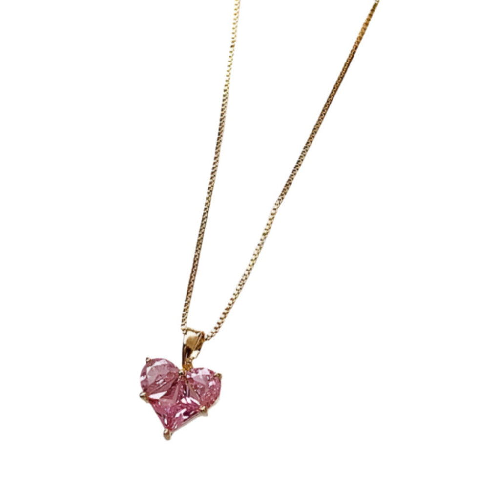 Gold necklace with a pink heart-shaped pendant on a white fabric background