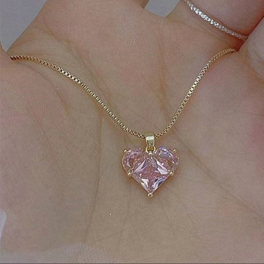 Gold necklace with a pink heart-shaped pendant held in a hand.