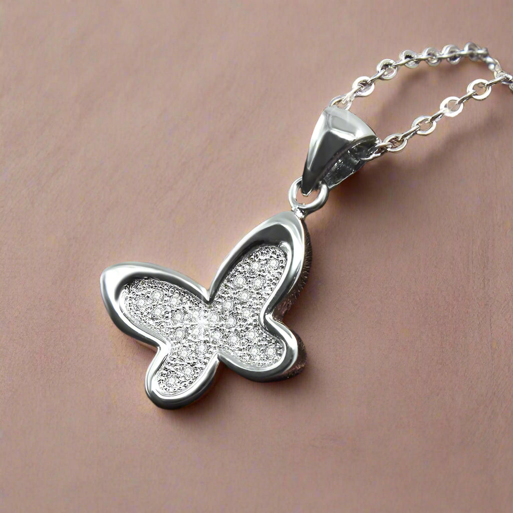 Butterfly-shaped silver pendant on a chain against a brown satin background