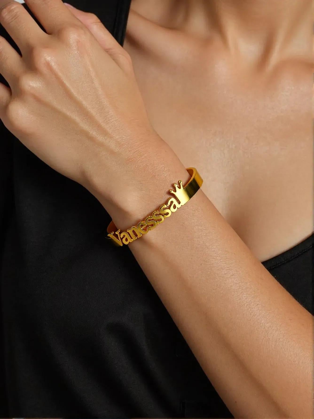 Gold bracelet with 'Vanessa' on a wrist against a black background