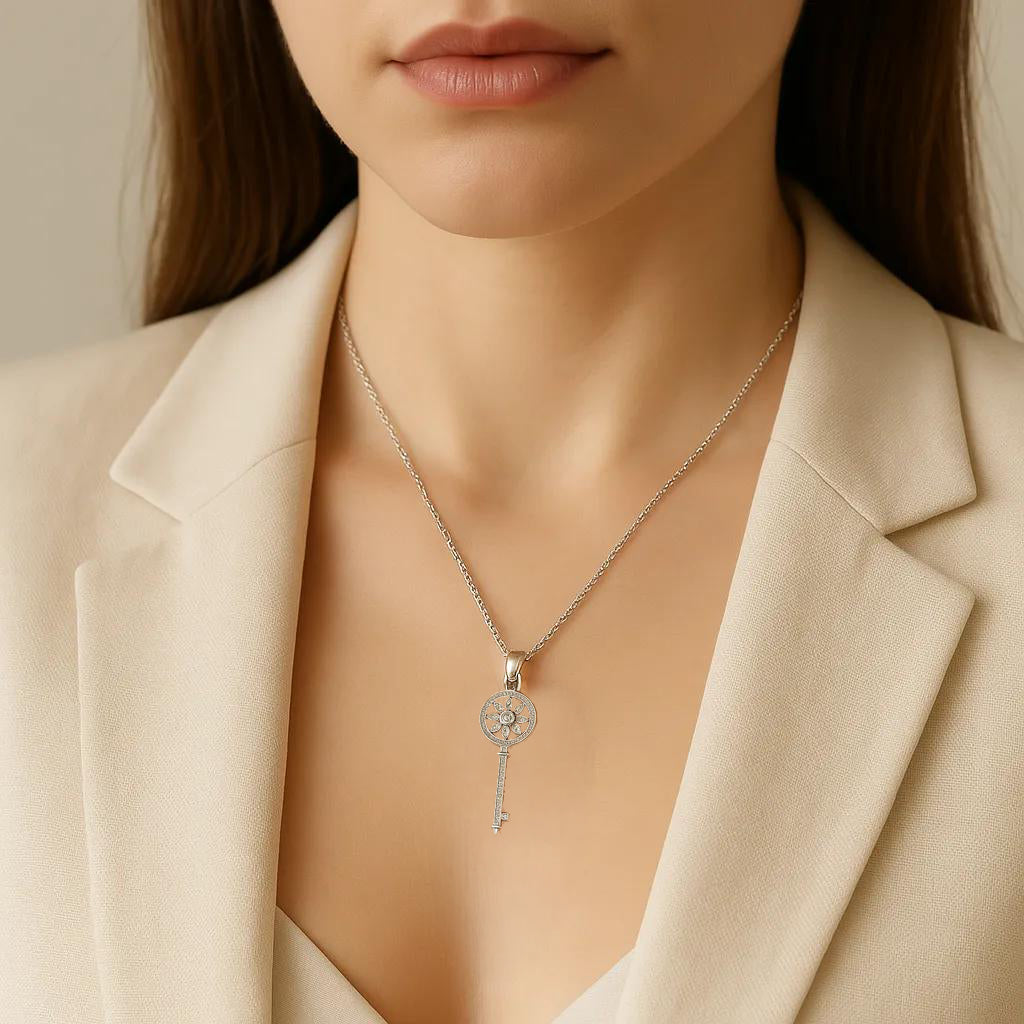 Necklace with a key-shaped pendant worn by a person in a beige blazer.