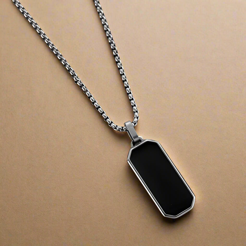 Close-up of men's silver stainless steel necklace with black enamel pendant"