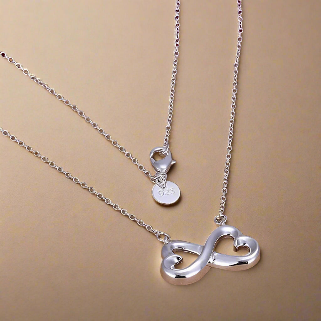 Sterling silver infinity-heart necklace on background.  
