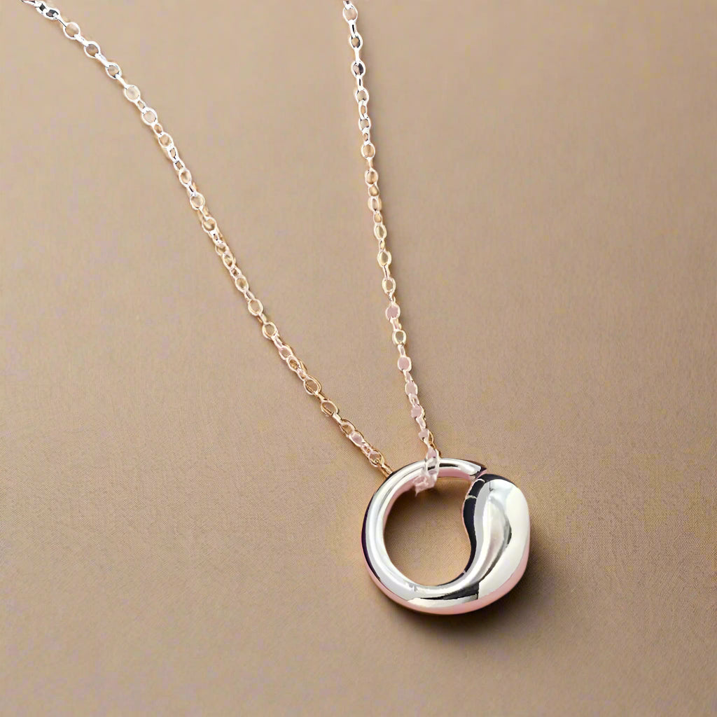 Minimalist silver pendant displayed elegantly on a surface.