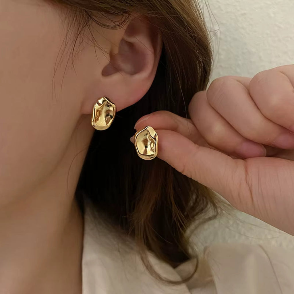 Gold sculptural stud earrings shown on model’s ear for scale and styling