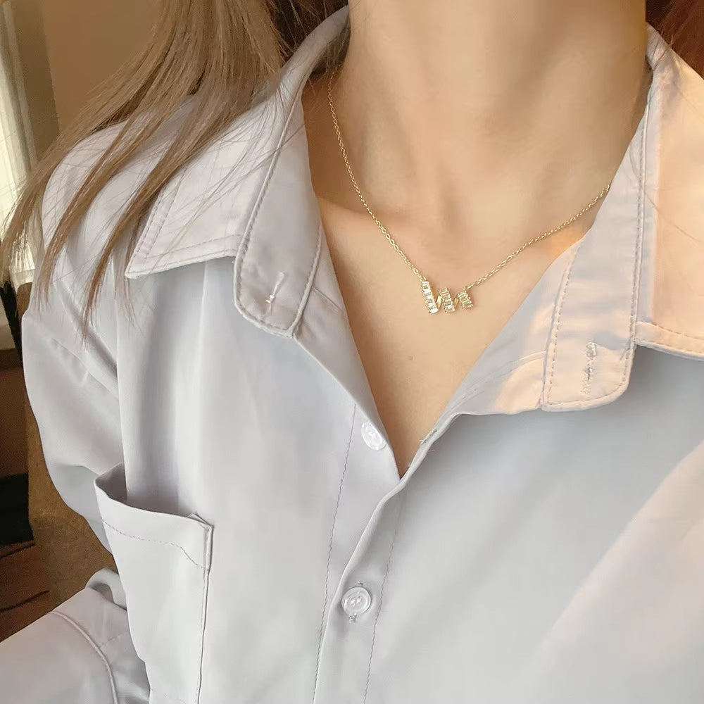 Person wearing a light gray shirt with a necklace featuring small rectangular pendants.