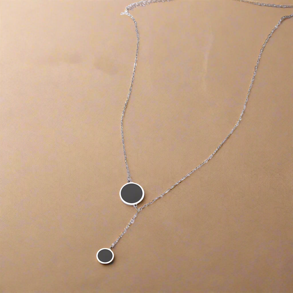 Silver Y-shaped necklace with double black enamel circles – close-up on model’s neck