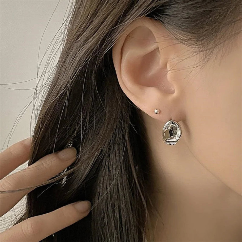 Close-up of molten-shaped earrings being held by hand for detail view