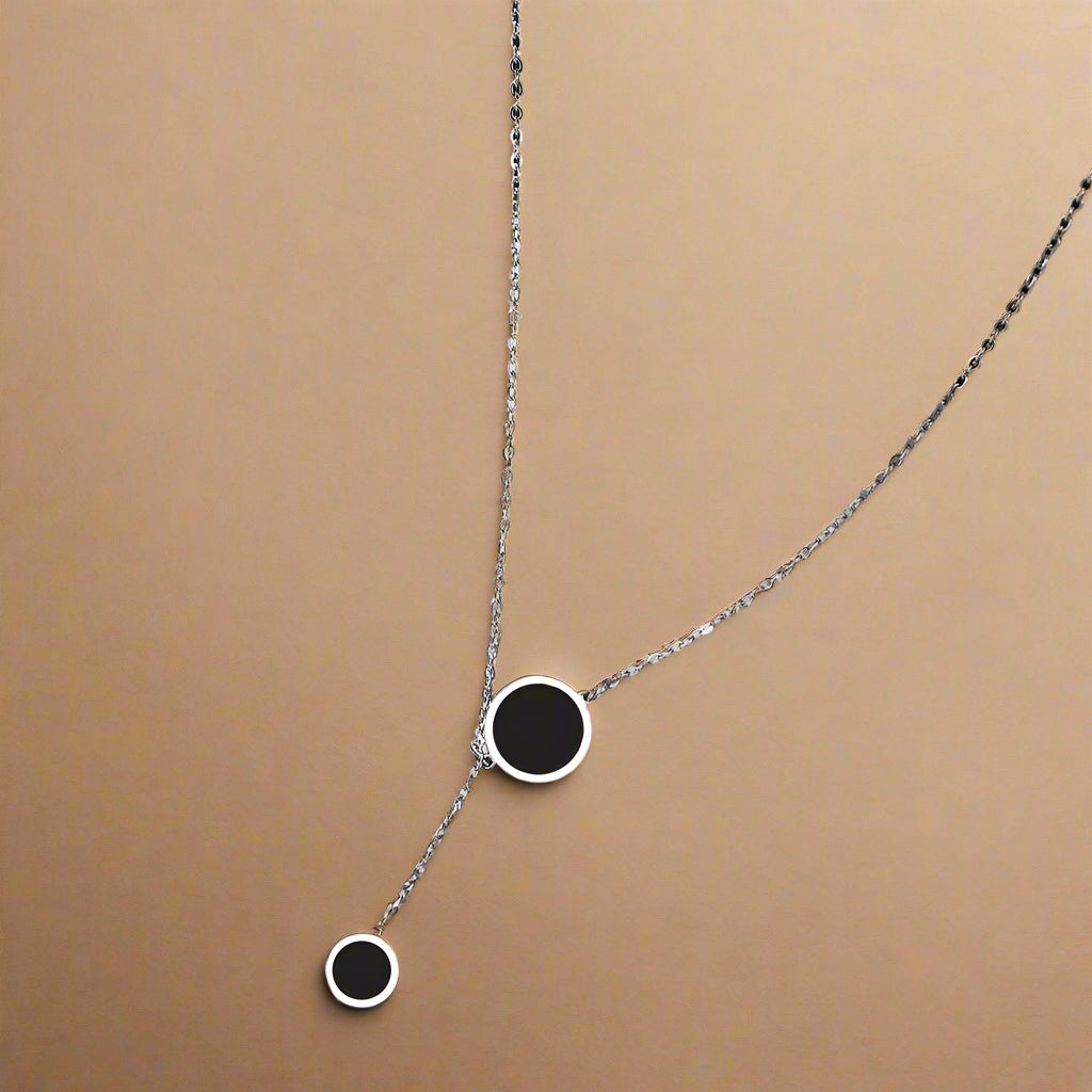 Silver Y-shaped necklace with double black enamel circles – close-up on model’s neck