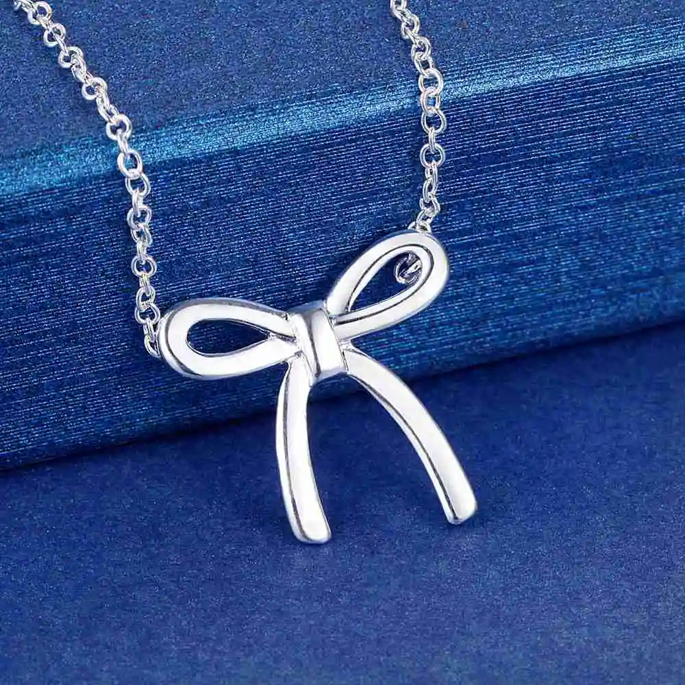 Sterling silver bow necklace on blue fabric.