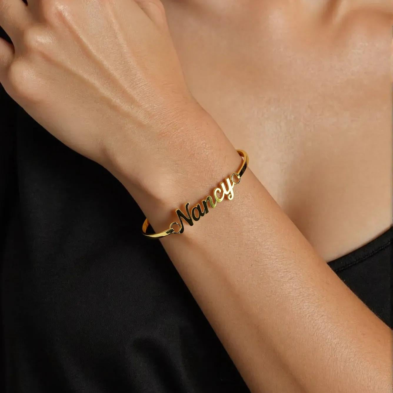 Gold bracelet with 'Nancy' engraved on a person's wrist against a black background