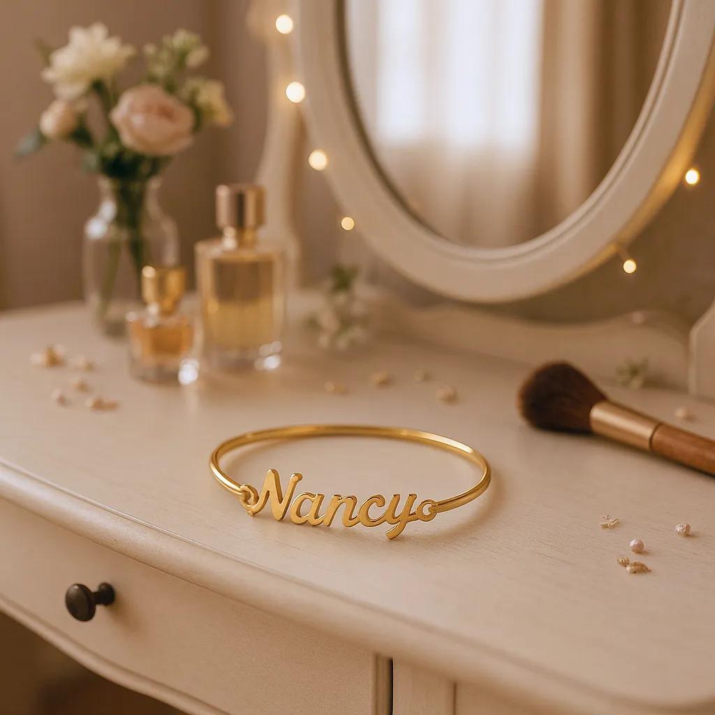 Gold bracelet with 'Nancy' on a vanity table with flowers and mirror.