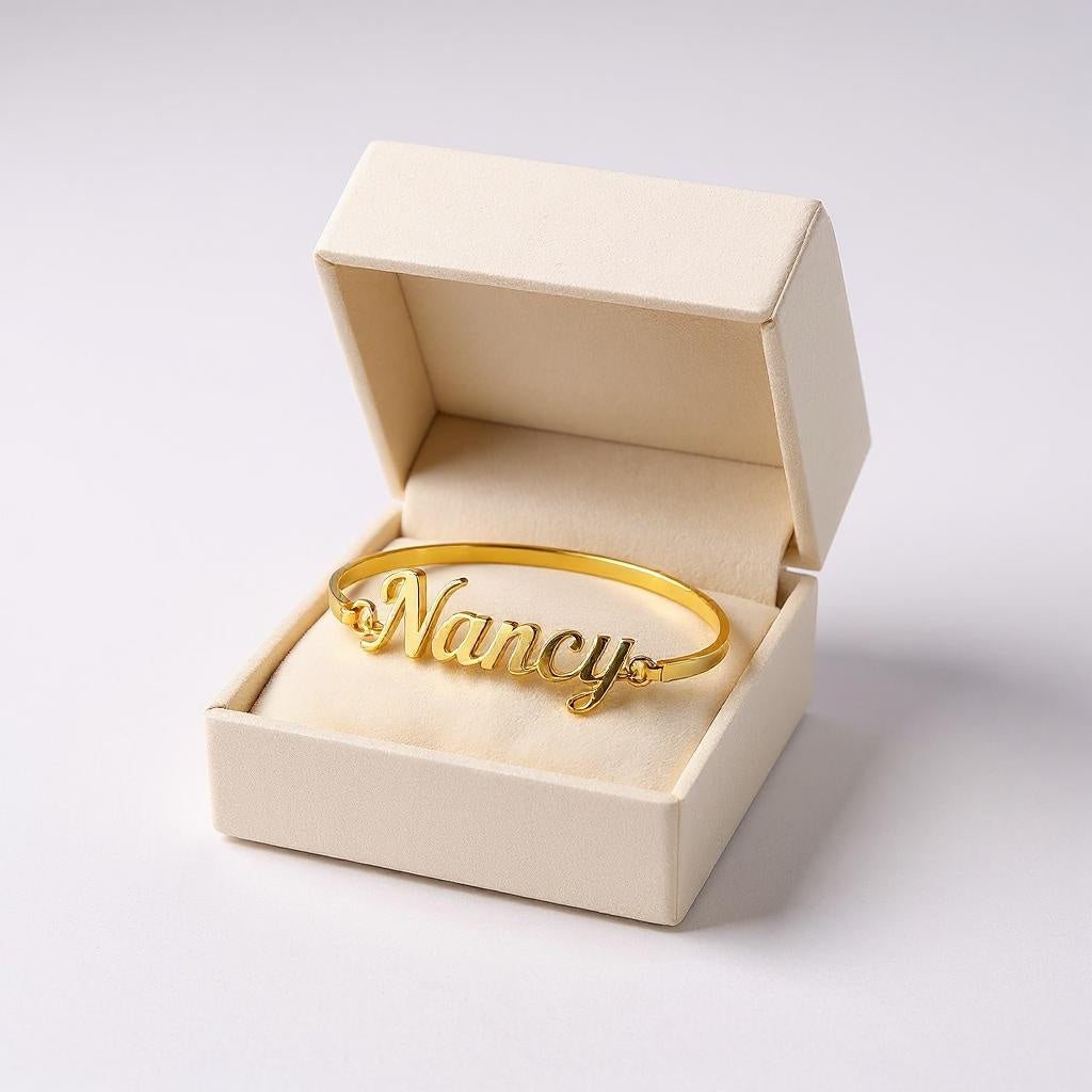 Gold bracelet with 'Nancy' engraving in an open beige box on a light gray background