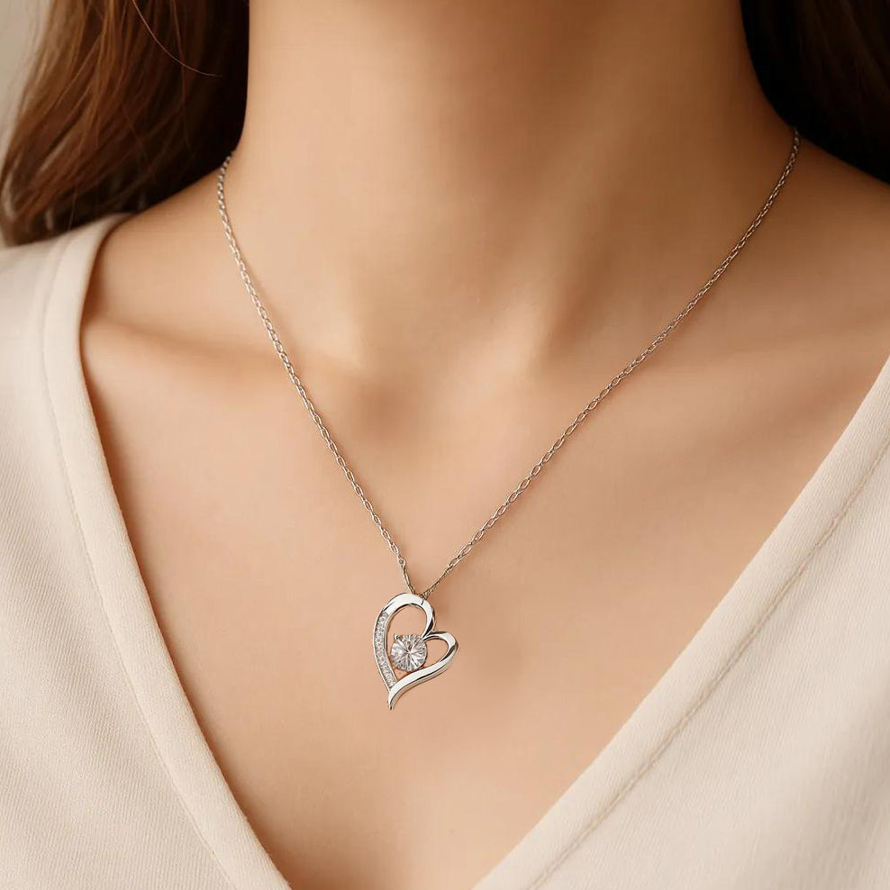 Silver heart-shaped necklace with a small heart pendant on a model wearing a beige top.
